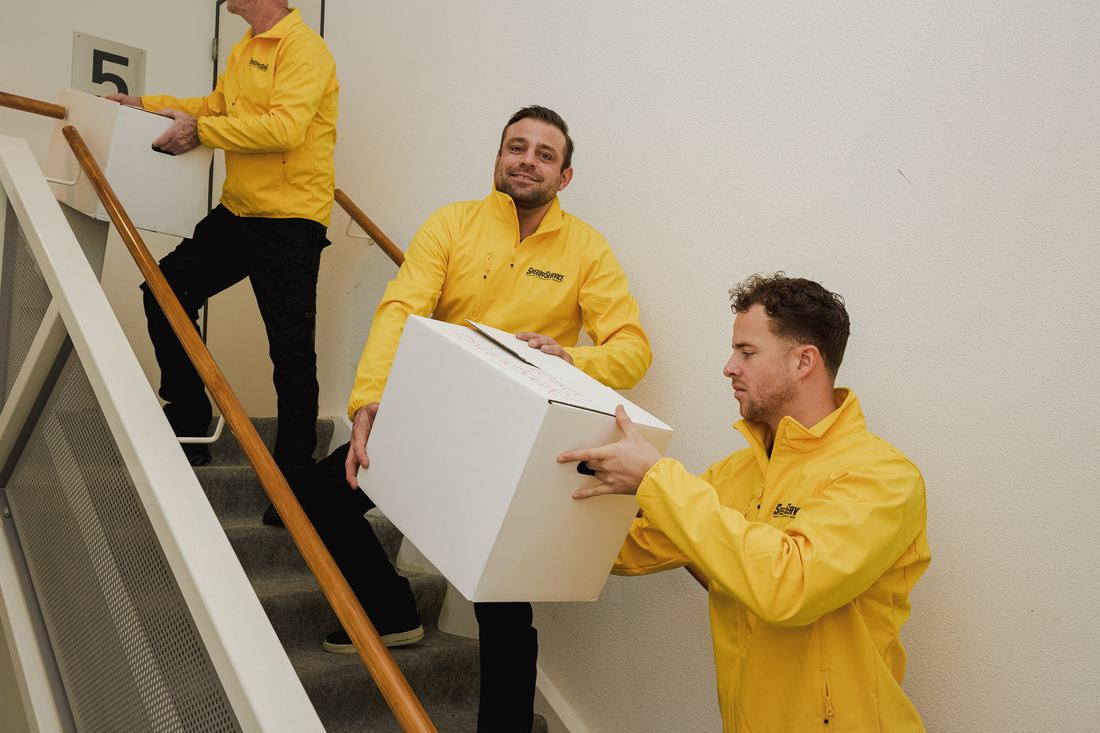 Drie verhuizers van SpeedyService dragen verhuisdozen omhoog door een trappenhuis
